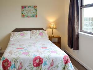 a bedroom with a bed with a floral bedspread at Beuchan Bungalow in Closeburn