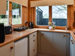 a kitchen with white cabinets and two windows at Algwen Cabin in West Walton