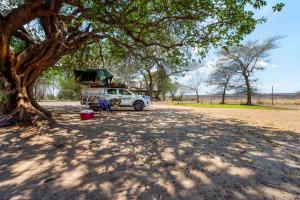 a white truck parked under a tree on a dirt road at Chobe River Campsite in Ngoma
