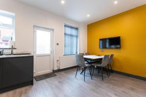 a dining room with a table and a tv on a yellow wall at Urmston House in Leigh