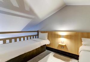 a bedroom with two beds and a nightstand between them at B&B HOTEL Dijon Marsannay in Marsannay-la-Côte