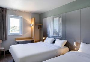 two beds in a hotel room with two windows at B&B HOTEL Lorient Caudan in Caudan