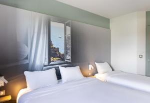 two beds in a room with a window at B&B HOTEL Lorient Caudan in Caudan