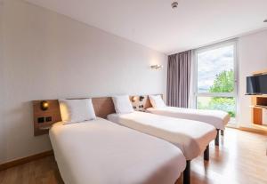 a row of beds in a room with a window at B&B HOTEL Lully 3 Lakes in Estavayer-le-Lac