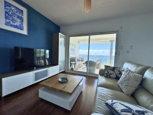 a living room with a couch and a tv and a table at Horizon Doré Appt avec piscine - vue sur mer in Gourbeyre