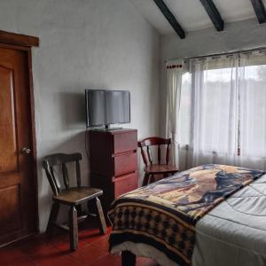 a bedroom with a bed and a tv and two chairs at Hospedaje Casa Campestre Pistacia Vera - Villa de Leyva in Villa de Leyva +11 photos