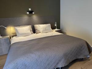 ein großes Bett mit einer grauen Decke und Kissen in der Unterkunft Hotel De Villa in Zelzate