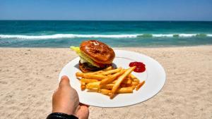 a sandwich and french fries on a plate on the beach at Ocean Camp in Al Qārin