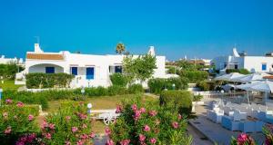 a white building with tables and umbrellas and flowers at Mapo Village Plaia in Villanova di Ostuni