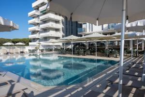 a swimming pool with chairs and umbrellas next to a building at Hotel Byron Bellavista in Lido di Jesolo