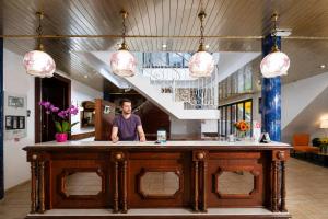 a man standing behind a bar in a lobby at Hôtel Hélianthe in Lourdes