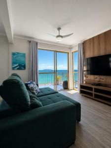 a living room with a green couch and a large window at Ingleses Palace Hotel in Florianópolis