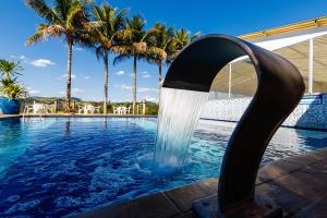 a water fountain in a swimming pool with palm trees at Cabanas do Morro in Serra Negra