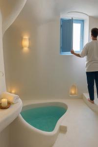a person looking out of a window in a bath tub at Urano Cave Suites in Santorini