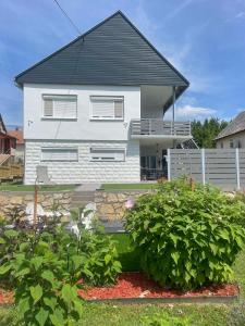 a white house with a black roof and some bushes at Víkend Apartmanok in Révfülöp