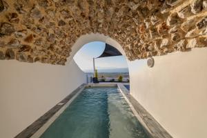 a pool in a house with a stone wall at Sun Angelos Oia - Luxury Cave Suites in Oia