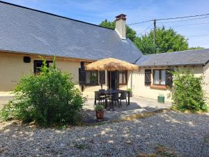 a house with a table and chairs under a straw umbrella at La Chaumière de Chabine in Oizon