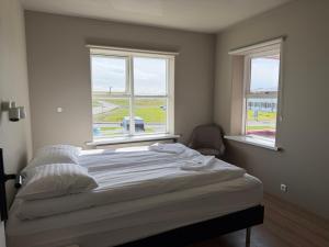 a bed in a room with two windows at Guesthouse Hvammur by the Harbour in Höfn