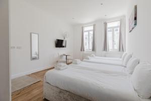 a white room with four white beds in it at The Hyde Hotel in London