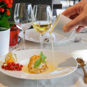 une personne verse du vin blanc dans une assiette de nourriture dans l'établissement Logis Hôtel restaurant Horizon 117, à Sentaraille