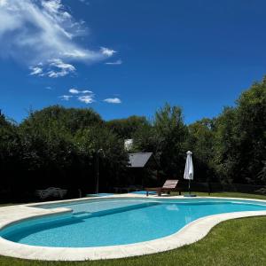 a swimming pool with an umbrella and a table and a bench at Complejo Inti Wara - frente al Río Los Reartes in Los Reartes