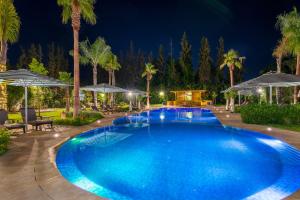 a pool at night with palm trees and umbrellas at Jnane Rihane Marrakech in Marrakesh