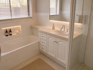a white bathroom with a tub and a sink and a bath tubermottermottermott at Charming & Spacious 5 Bedroom Bayside House with Pool in Birkdale +3 photos