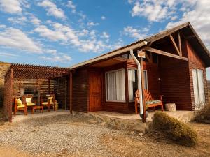 a small wooden house with a porch and chairs at Viento Sur Astro Camping & Cabañas in Los Hornitos