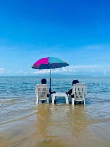 two people sitting in chairs under an umbrella on the beach at Pornaree Hotel in Ban Pak Ba Ra