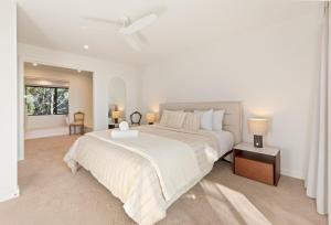a white bedroom with a large bed and a window at Perfectly Pambula in Pambula Beach