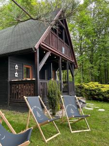 two lawn chairs and a house with a building at Domek Pod Lasem in Trzciana