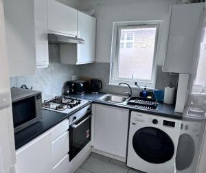 a kitchen with white cabinets and a sink and a microwave at Watford Junction Stay in Watford