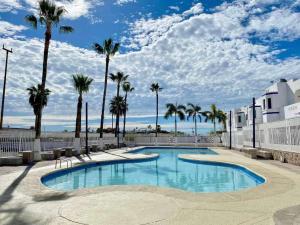 a swimming pool with palm trees and a cloudy sky at Depa 224pa con terraza alberca in San Carlos