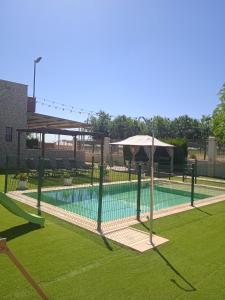 a swimming pool with an umbrella and a tennis court at Casa Rural Kentia in Valdepeñas