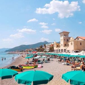 a beach with blue umbrellas and people on the beach at Blu Marine Loano -Terrazza Vista Mare- in Loano