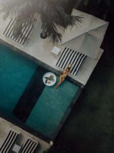 a woman is sitting in a swimming pool with an umbrella at White Palm Uluwatu - Wellness & Recovery Retreat - 2 Min Walk to Balangan Beach in Jimbaran