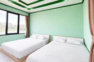 two beds in a room with green walls and windows at Cozzy Malakai Guesthouse in Palayangan