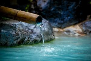 a pipe with water pouring out of it into a river at Okamotoya in Beppu