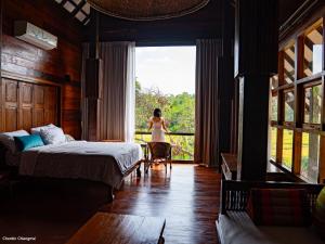 a woman standing in a bedroom looking out the window at บ้านริมดอย แม่ริม in Ban Mae Raem