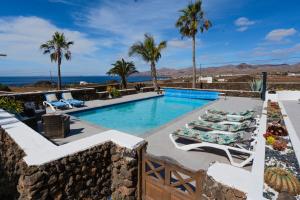 a pool with chairs and palm trees and the ocean at Villa Las Palmitas - Sea Views - Private Pool - Hot Tub - Table Tennis in Puerto Calero