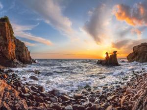 two people standing on a rocky beach at sunset at The Apple Garden in Allinge