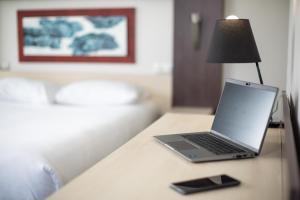 a laptop on a table with a lamp and a cell phone at Elema Hotels Beauvais ex Hostellerie Saint Vincent Beauvais Aeroport in Beauvais