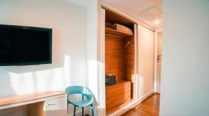 a room with a tv and a blue chair and a closet at Hotel Vértice Chipiona Mar in Chipiona