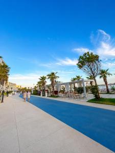 people walking down a blue sidewalk with palm trees at ALZETA Aparthotel in Durrës