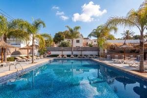 a swimming pool with chairs and palm trees in a resort at Hotel Chevy & Suites in Cala Ratjada