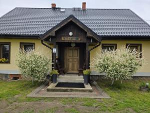 a yellow house with a wooden door and two trees at PRZYSTANEK nowEKOprzywno - Żółty Domek Pod Kasztanem in Barwice