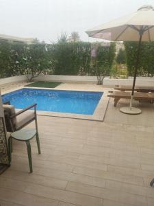 a swimming pool with an umbrella and a table and benches at Luxury Salalah Villa in Salalah +6 photos