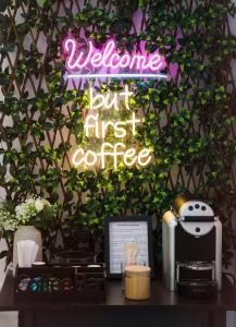 a neon sign that says welcome but first coffee at Apartment Simply 206 in Gázion