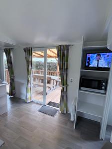 a living room with a tv and a sliding glass door at Bungalow Camping 4 étoiles in Messanges