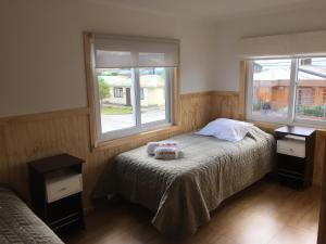 a small bedroom with a bed and two windows at Hostal Andes Patagonicos in Puerto Natales